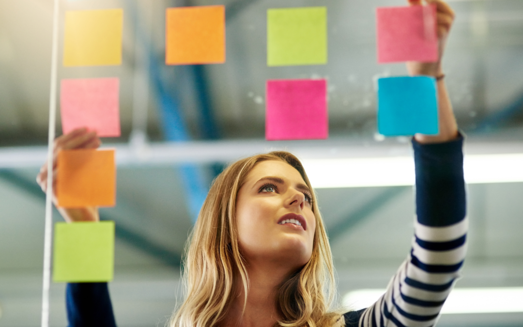 priority management blog post image of woman putting colored sticky notes on glass wall