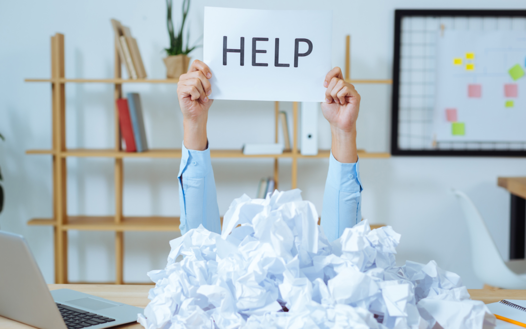 hands holding up help sign under piles of paper