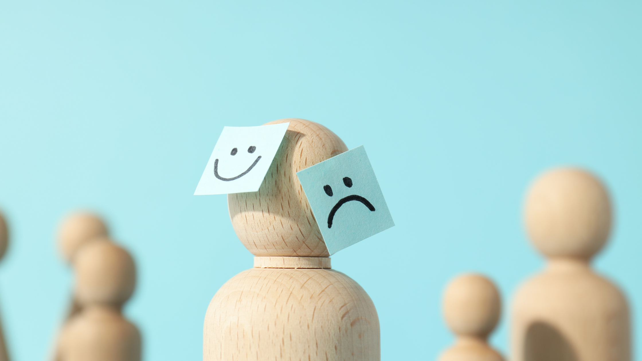 wooden figure with sad and happy faces on paper attached