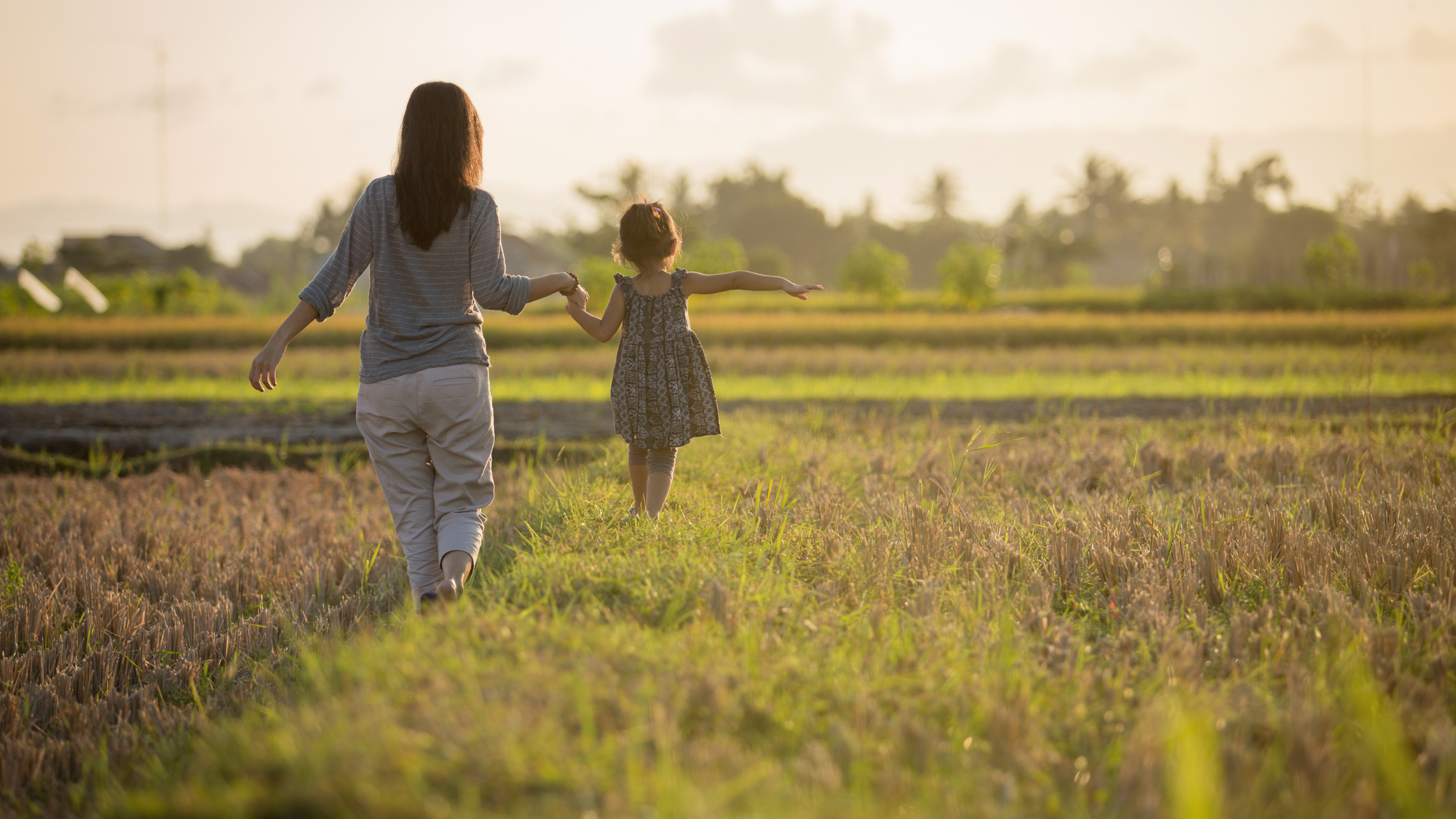 woman and girl walking away into the sun in a field